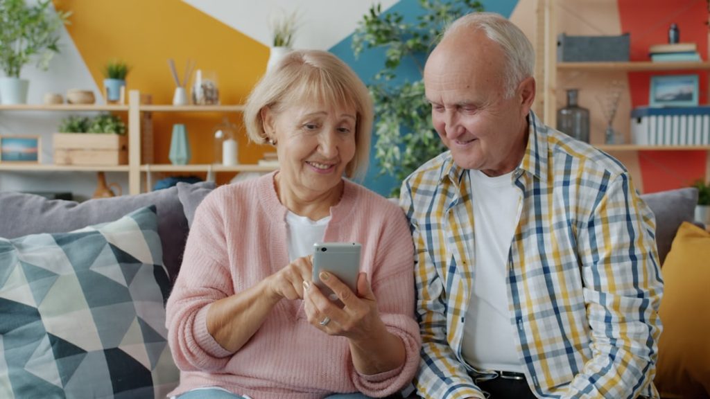 elderly-couple-looking-at-a-smartphone-together-gefm1m8kyji Old woman using smartphone touching screen relaxing on couch with senior husband in modern apartment. Technology, retirement and lifestyle concept.